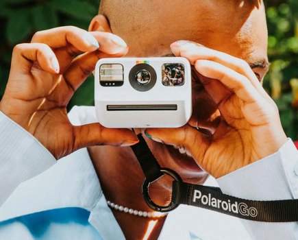 Photograph of a man using small white Polaroid Go instant camera, holding the viewfinder up to his eye